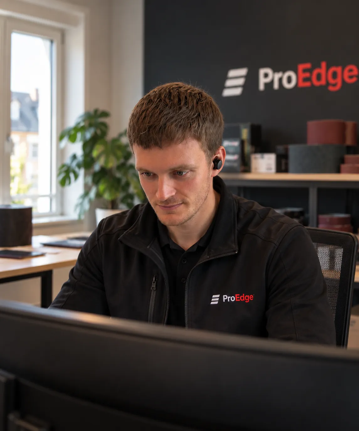 Medarbejder hos ProEdge ved skrivebordet med slibebånd på hylden bagved